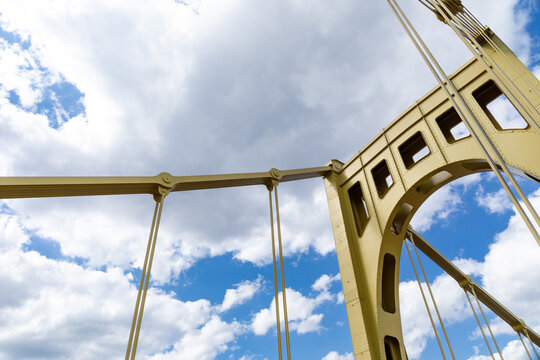 Yellow suspension bridge structure against a bright blue sky with white clouds, horizontal aspect