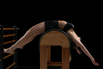 Woman doing pilates exercises in a barrel equipment, black backgound, low key.