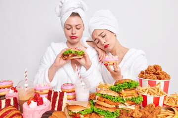 Unhappy young women tempting to eats something delicious surrounded by junk food keep to diet and healthy nutrition feel hungry look sadly at tasty burger sweet doughnut. Overeating concept.