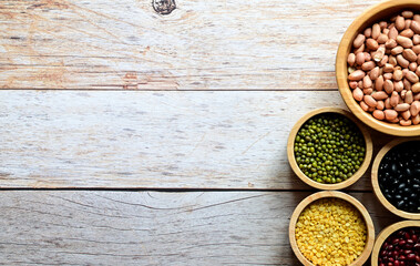 Dried peanuts, Hulled-split Mung Bean (Yellow beans), Mung Beans, Red beans, Black Beans, Millet grains are in the wooden bowl on the wooden table.