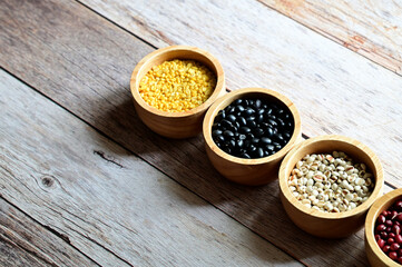 Dried peanuts, Hulled-split Mung Bean (Yellow beans), Mung Beans, Red beans, Black Beans, Millet grains are in the wooden bowl on the wooden table.