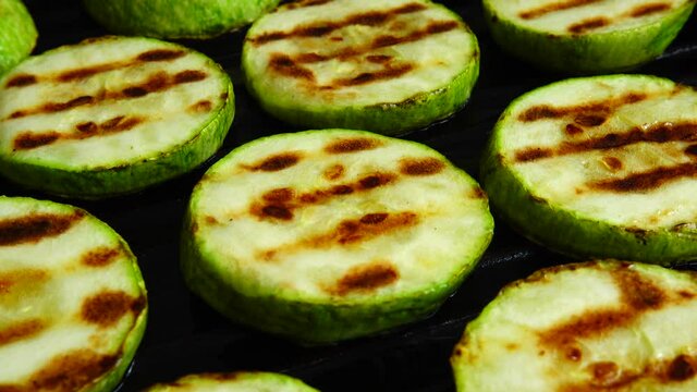 Fried zucchini slices rotate in a grill pan.