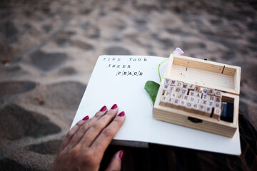 A female hand holding a travel journal with a flower and stamping kit with alphabet on her lap....