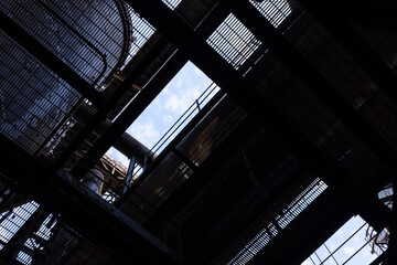 View looking up and out from a dark industrial space through grids and furnaces to blue sky beyond,...