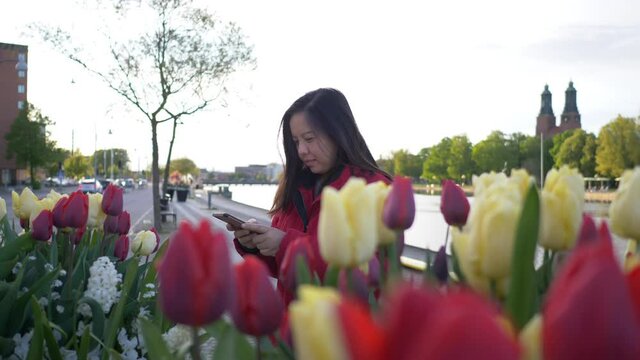 Asian woman walking and sitting to take a picture of beautiful flowers in the city, getting wonderful time, feeling relax and seeing beautiful nature. City park background. Going out for a walk