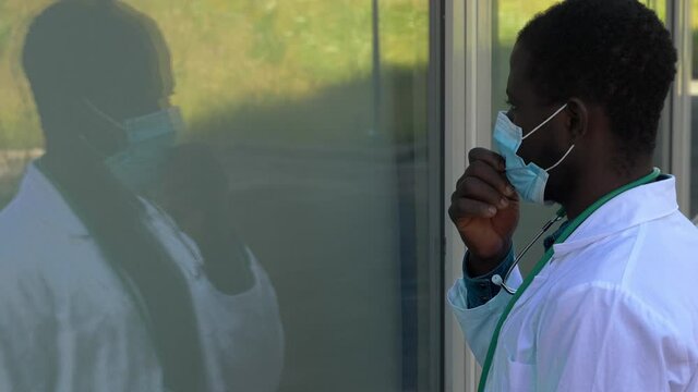 Black Doctor Looks At His Reflection On The Glass And Pulls Down His Mask