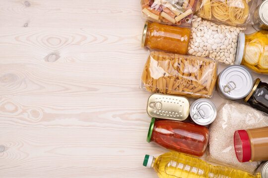 Food donations such as pasta, rice, oil, peanut butter, canned food, jam and other on white wooden table, top view with copy space 