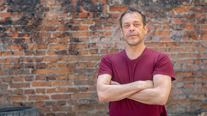 Portrait of a serious elderly man with a strong build of 45-50 years old in a T-shirt on the background of a brick wall. Maybe he's an actor or a construction worker.