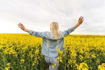 Naklejka na ściany i meble Woman with yellow flowers. Summer portrait of female in rapeseed field