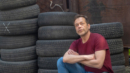 Portrait of a man with a strong build of 45-50 years old against the background of old car tires and a brick wall.Concept: hard work of an immigrant, working in an auto repair shop.