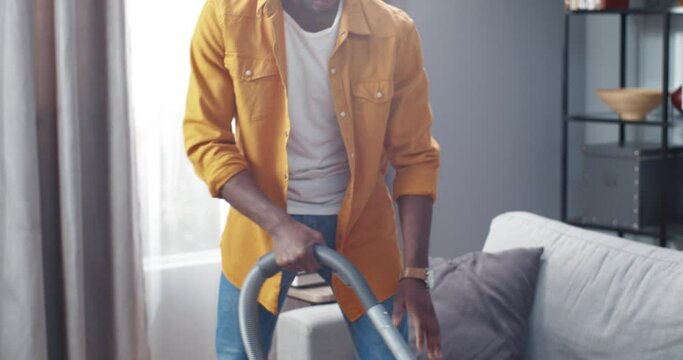Close up of young stylish african american man concentrating vacuuming carpet in living room focused on cleaning process.