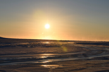 Arctic landscape in winter time. Small river with ice in tundra. Sunset.