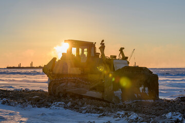 Yellow tractor in winter tundra. The road construction. Bulldozer.