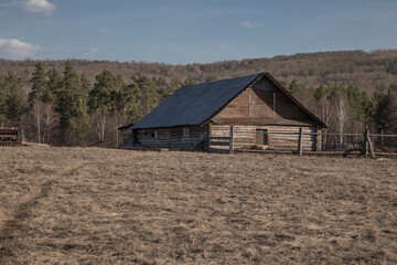 An old wooden house stands against the backdrop of mountains and forests. Rustic rural landscape. Beautiful mountains. Blue sky. Sunny day.