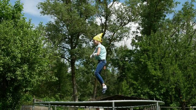 4K colorful spring or summer video footage. A little girl, scholl girl with a broken arm in a plaster cast jumps merrily on a trampoline. Child having fun while on holiday in a country house