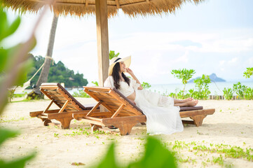 A young woman relaxing and sitting on the lounge chair looking at beautiful beach on holidays