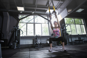 Obraz na płótnie Canvas Low angle shot of a female athlete doing squats with trx trainer at sport studio, copy space