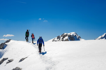three climbers walk along the snow-capped ridge of a summit in the Slovenian Alps