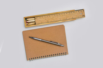 Colored pencils and ruler box with pens and notebooks on gray desk.
