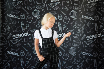 interesting smiling little girl in school clothes against a school board with drawings on the theme of School.  School concept. Back to school.