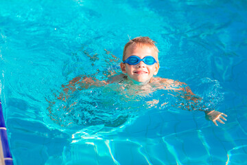 Naklejka premium Cute happy little boy in goggles swimming and snorking in the swimming pool