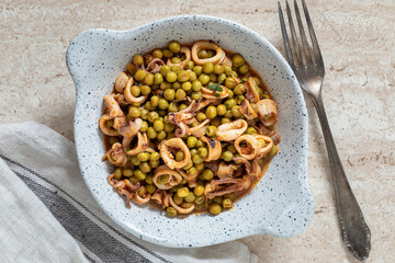 A plate with calamari and green peas. From above.