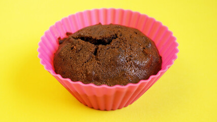 Close up against a yellow background is a gluten-free, home-made chocolate cake with apples in a pink silicone mold. side view