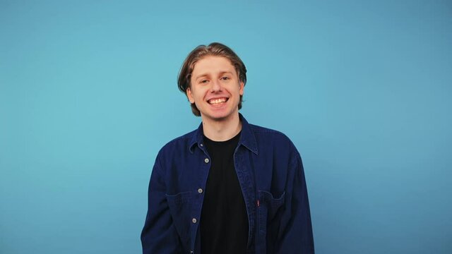 Positive young man stands on a blue background and gives a fist to a friend and looks at the camera with a smile on his face.