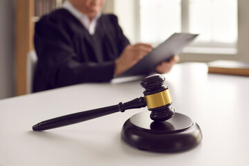 Close up of a dark brown judge gavel on a table against the backdrop of a judge reading a verdict....