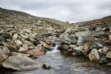 Stream surrounded by rocks. Fresh water is coming out of the massive mountain.