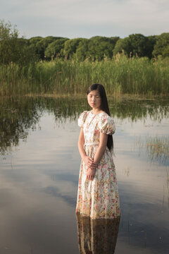 Young woman standing in the water in a lake wearing classic flower dress 