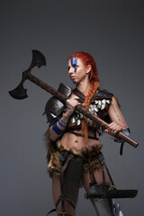 Fototapeta na wymiar Beautiful martial woman with axe and armored clothing in gray background