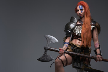 Brave and powerful woman viking with axe posing in gray background - obrazy, fototapety, plakaty