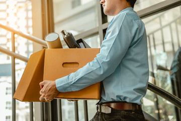 Businessman is carrying a brown cardboard box to resignation - obrazy, fototapety, plakaty