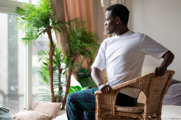 Sporty young african man practicing yoga using chair, doing Revolved Chair Pose, Parivrtta...