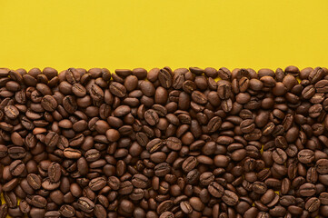 Roasted coffee beans on yellow background with copy space. Close up top view.