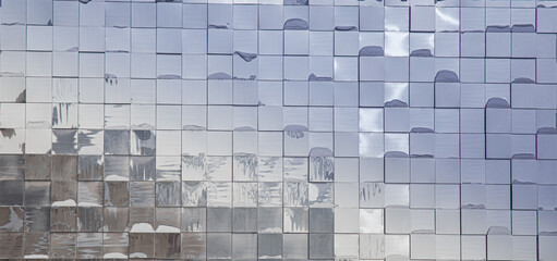The glass mirrored surface of the facade of the modern building in the appearance of square plates...