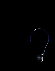silhouette of a light bulb on a black background, subtle light outlining an extinguished light...