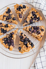 Homemade oatmeal scones with berries stacked on cooling rack on white wooden background. Vegan sweet baked food. Gluten free pastry.