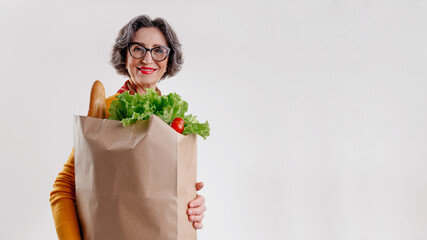 Happy senior woman holding paper bag with fresh vegetables