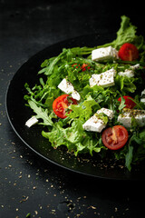 Fresh salad with arugula, cherry tomatoes and feta cheese on a dark background