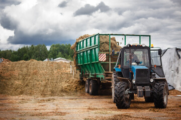 A tractor with a large trailer, unloads the silage into a trash.