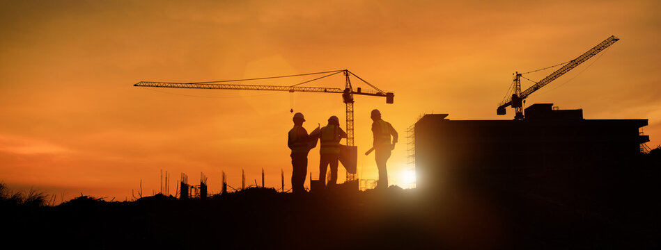 Silhouette engineer construction work control and tower crane background on natural sunset sky.,Heavy industry and building construction work concept in banner
