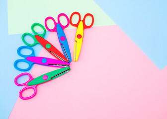 Children's safe scissors lie on a colorful background with a place for an inscription