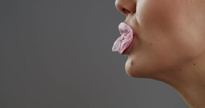 Young woman popping bubble gum on grey background, closeup
