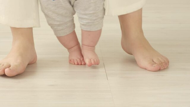 Baby's feet taking steps learning to walk with mothers help. Child 6 months of age.
