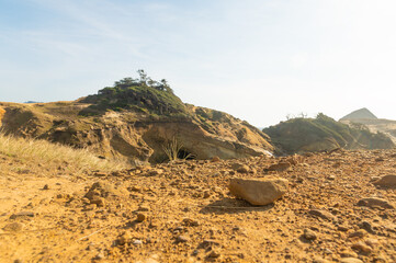 In the photo we see a sand dune, a small sandy hill. At the top of the hill, grass dried from the hot sun. Clear blue sky. In the foreground is a sandy stone. No people. Place for your insert.
