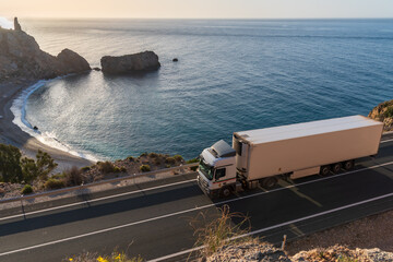 Truck with refrigerated semi-trailer driving along a road by the sea with a beach in the background.