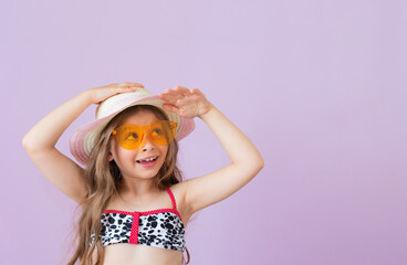 A pretty little girl in a bathing suit and sunglasses put her hands on her hat.