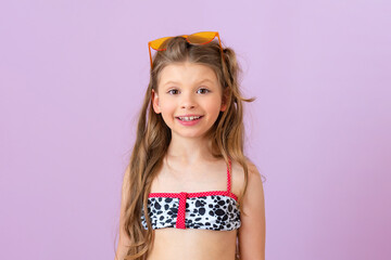 A beautiful little girl in a swimsuit poses on a purple isolated background.